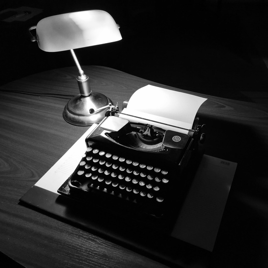 A Black Typewriter Beside a White Table Lamp